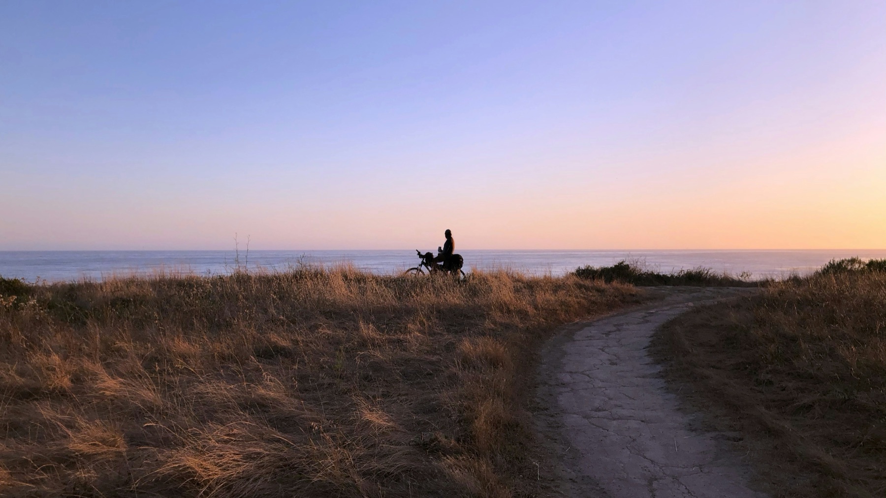 A cyclist pausing along a Goleta coastal bluff trail at sunset